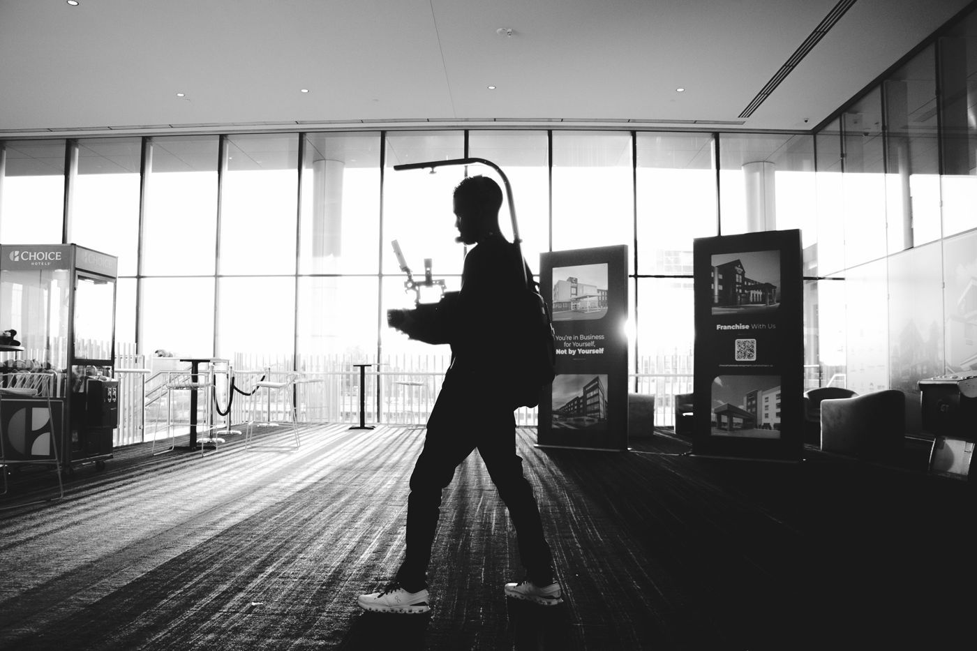 A crew member crossing an expo hall with a gimbal, in black and white