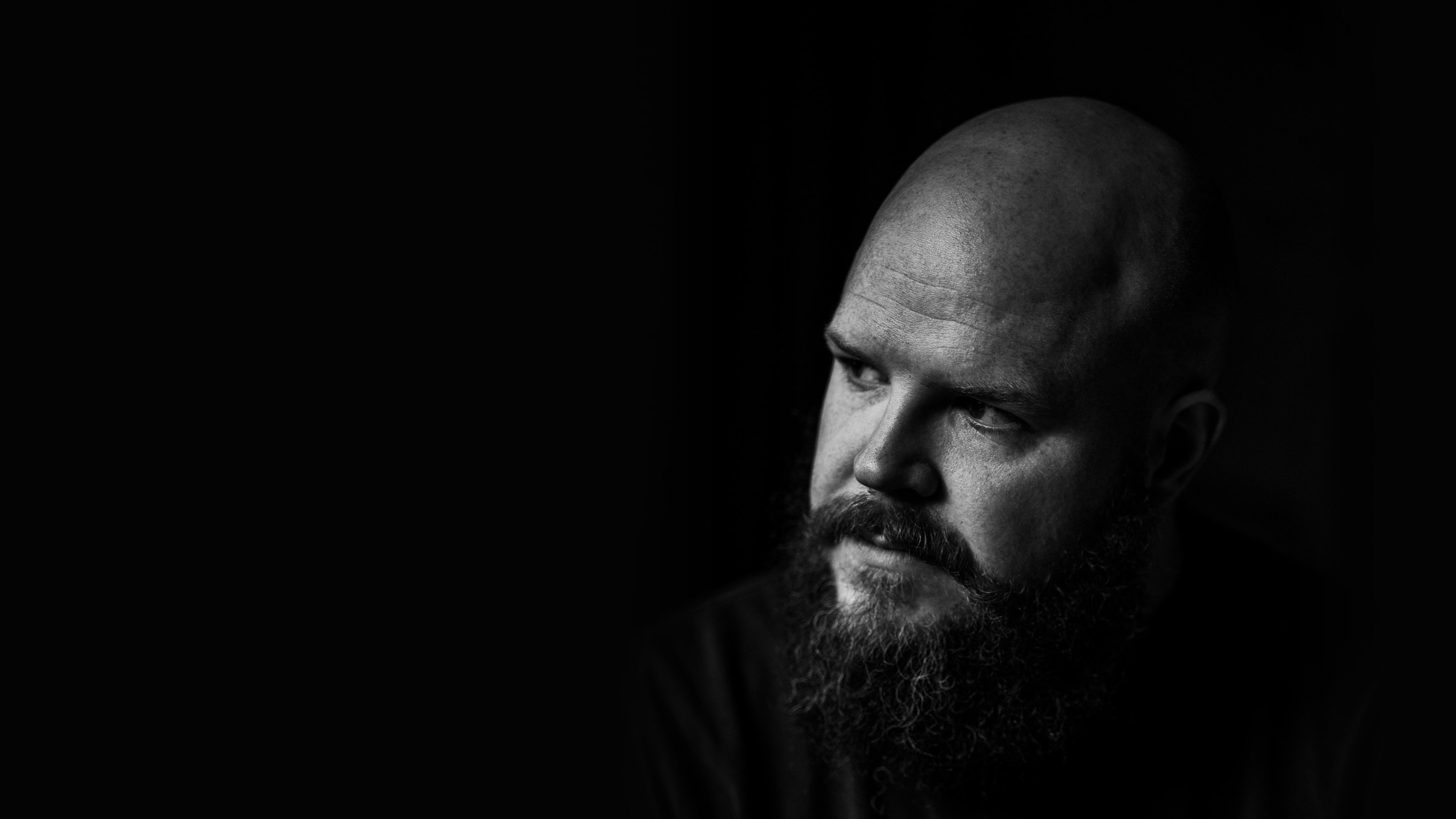 A bearded man in dramatic side light on a black background, in black and white